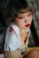 A woman in a white shirt and red lipstick sitting on a bed.