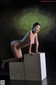 A nude woman sitting on top of a white box.