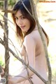 A naked asian woman leaning against a tree branch.