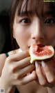 A woman eating a fig in front of her face.