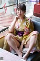 A woman in a kimono sitting on a couch next to a window.