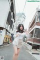 A woman in a white shirt and beige skirt walking down a street.